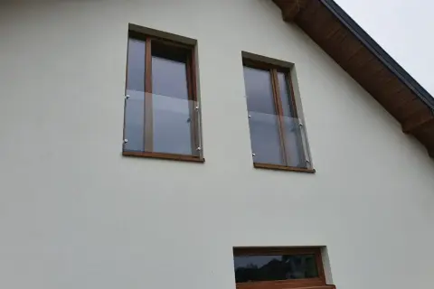 Dwa okna z drewnianymi ramami i szklanymi balustradami na białej ścianie domu.