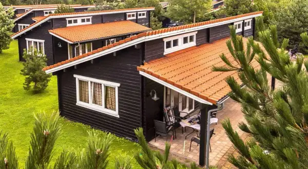 Czarny bungalow z pomarańczowym dachem, otoczony zielenią. Idealne miejsce na wypoczynek, zastanawiasz się bungalow co to?