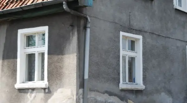 Szare ściany domu z białymi, tradycyjnymi okna skrzynkowe. Dach pokryty czerwona dachówką.