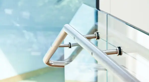 Nowoczesne mocowanie balustrady od czoła do szklanej tafli. Metalowy uchwyt pewnie trzyma się szkła, zapewniając bezpieczeństwo.