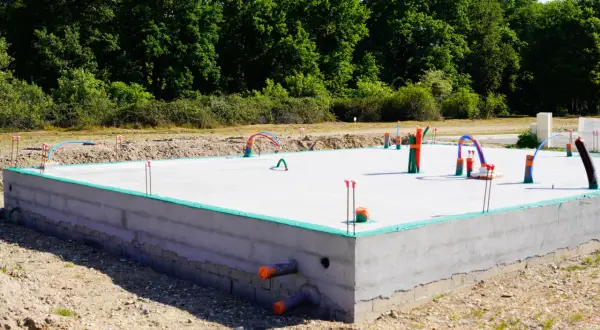Nowa płyta fundamentowa z wystającymi rurami i instalacjami, gotowa na dalsze prace budowlane.