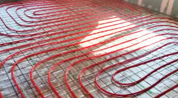 Instalacja podłogówki. Czerwone rurki systemu grzewczego ułożone na siatce. Cena za m2 robocizny jest kluczowa dla budżetu.