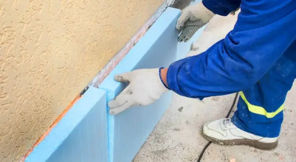 Ręce w rękawiczkach układają niebieski styropian na fundamencie. To kluczowy etap budowy, by wybrać odpowiedni styropian na fundament.