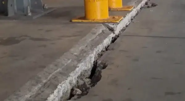 Pęknięcie w betonowej posadzce z widocznymi podporami przemysłowymi w tle.