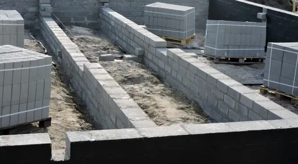 Budowa fundamentów z bloczków betonowych, widoczna izolacja pozioma fundamentów. Materiały budowlane czekają na użycie.
