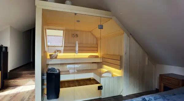 Nowoczesna sauna w domu, wykonana z jasnego drewna, z przeszklonymi drzwiami i nastrojowym oświetleniem. Idealne miejsce na relaks.