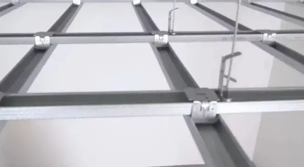 Sufit podwieszany krzyżowy z białymi panelami i metalową konstrukcją. Widać system profili, który tworzy siatkę, a nie pojedyncze belki.