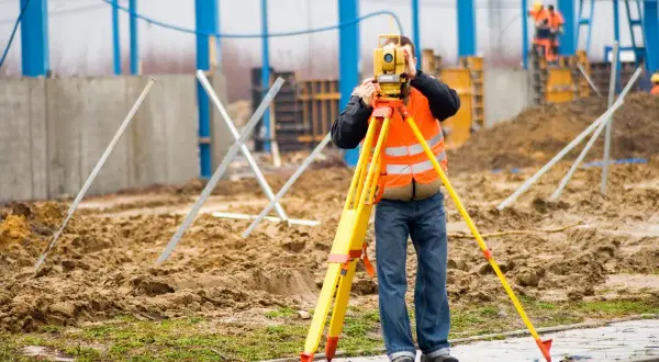 Na budowie technik geodeta w kamizelce odblaskowej mierzy teren za pomocą niwelatora.