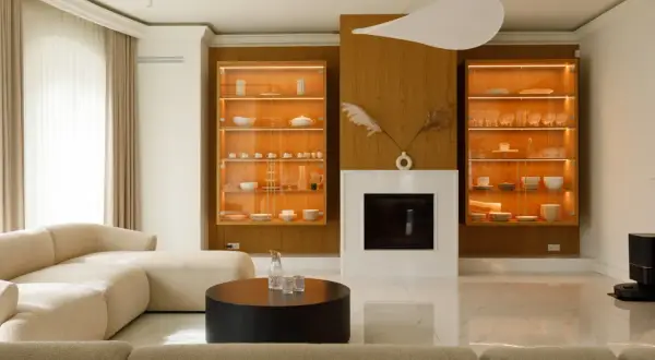 Nowoczesny salon z kominkiem, przeszklonymi witrynami i beżową sofą.