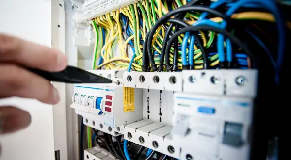 Ręka majstruje przy bezpiecznikach, tworząc instalację elektryczną w domu. Kolorowe przewody tworzą plątaninę.