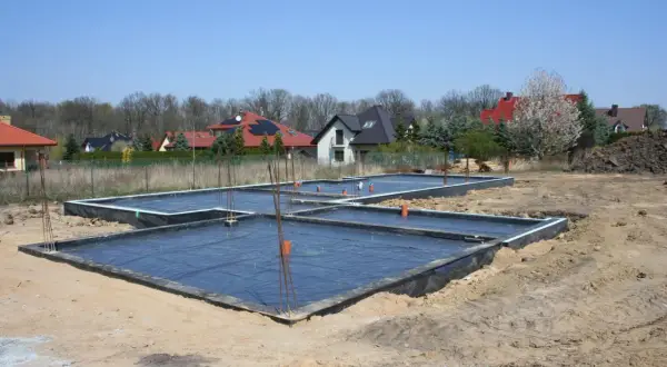 Fundament płyty fundamentowej w budowie, z czarną folią i zbrojeniem.
