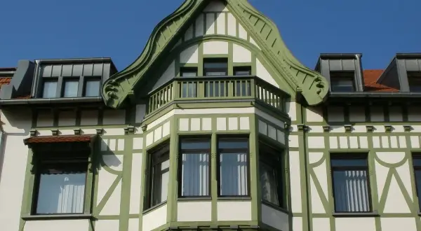 Elegancki ryzalit co to? Wystający fragment fasady budynku, ozdobiony zielonymi elementami i balkonem, z charakterystyczną, falistą formą dachu.