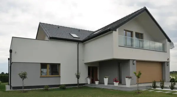 Nowoczesny dom z dwuspadowym dachem i balkonem. Elewacja w odcieniach bieli i szarości, z drewnianą bramą garażową. Świetny pomysł na elewację domu.