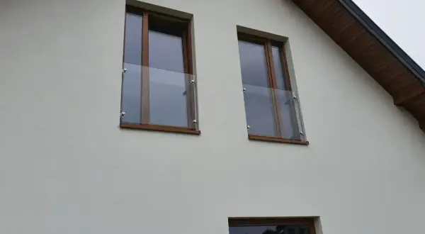 Dwa okna z drewnianymi ramami i szklanymi balustradami na białej ścianie domu.