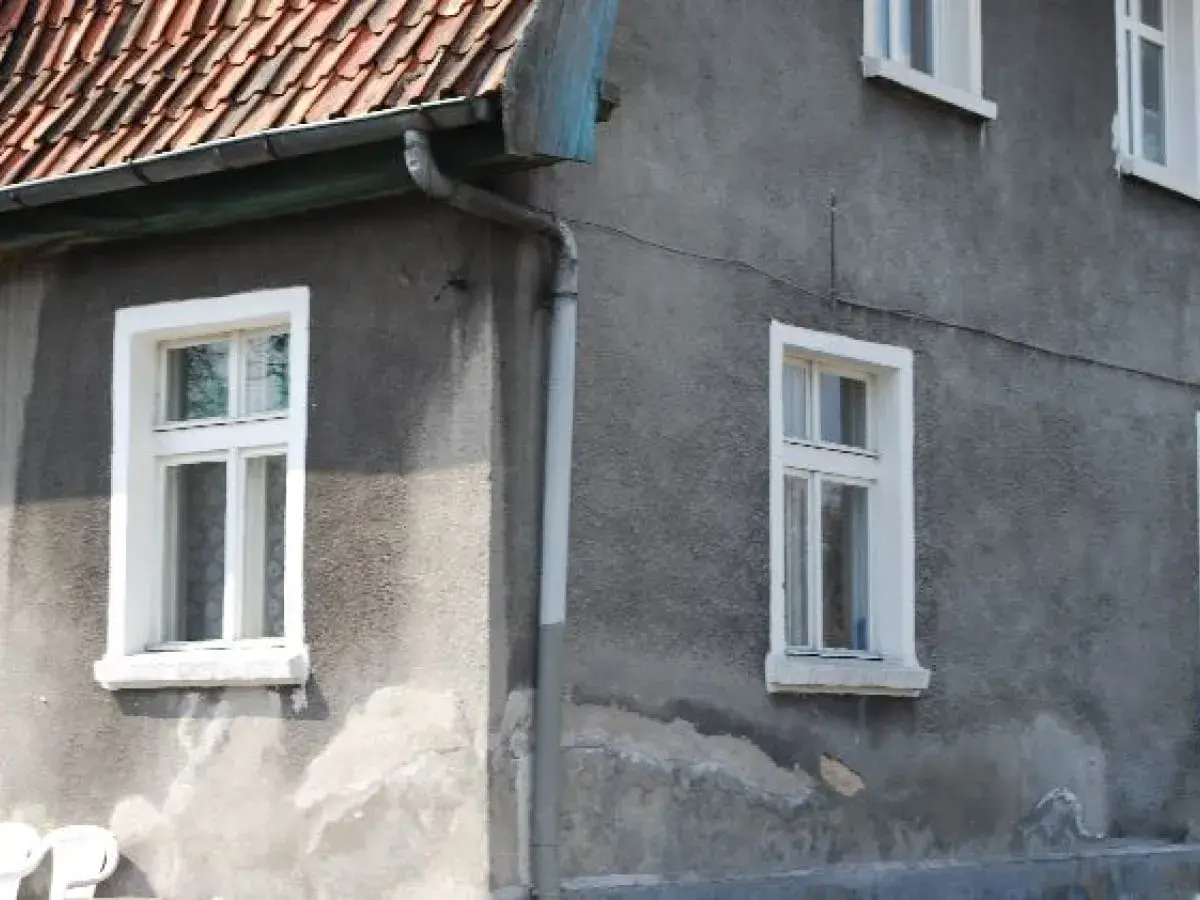Szare ściany domu z białymi, tradycyjnymi okna skrzynkowe. Dach pokryty czerwona dachówką.