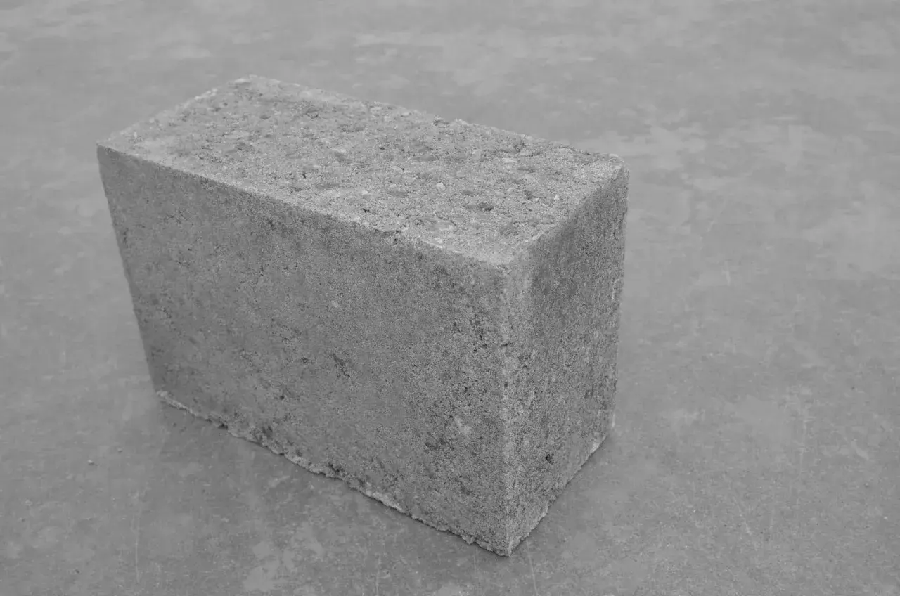 Szary bloczek betonowy na szarym tle. Jego wymiary są standardowe, idealny do budowy.