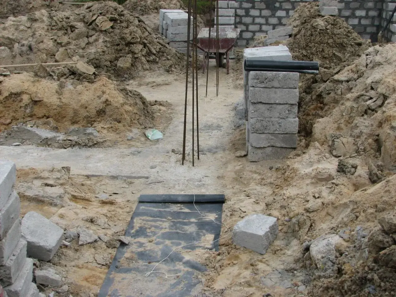 Budowa domu w toku. Widać wykopy, zbrojenie i materiały budowlane. Fundament czeka na zalanie.
