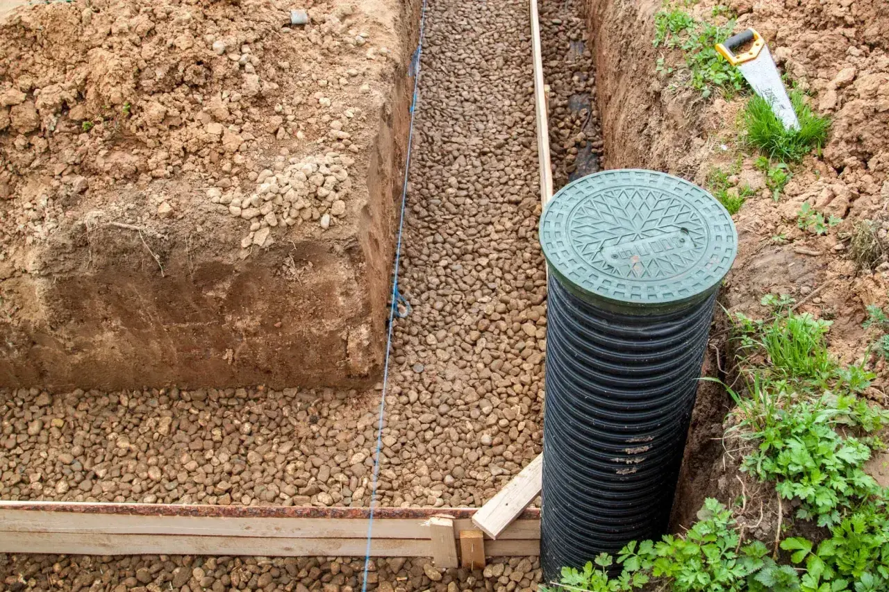 Wykop pod fundamenty z żwirem, rurą drenarską i zieloną pokrywą rewizyjną.