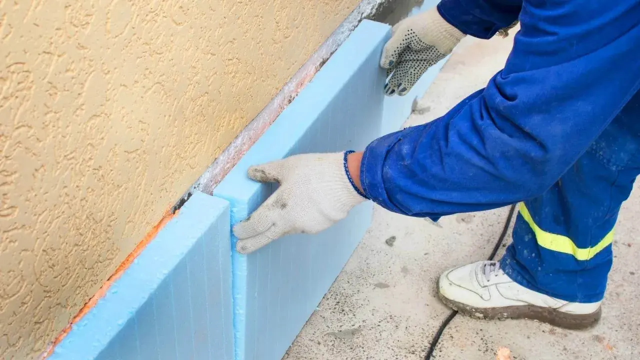 Ręce w rękawiczkach układają niebieski styropian na fundamencie. To kluczowy etap budowy, by wybrać odpowiedni styropian na fundament.