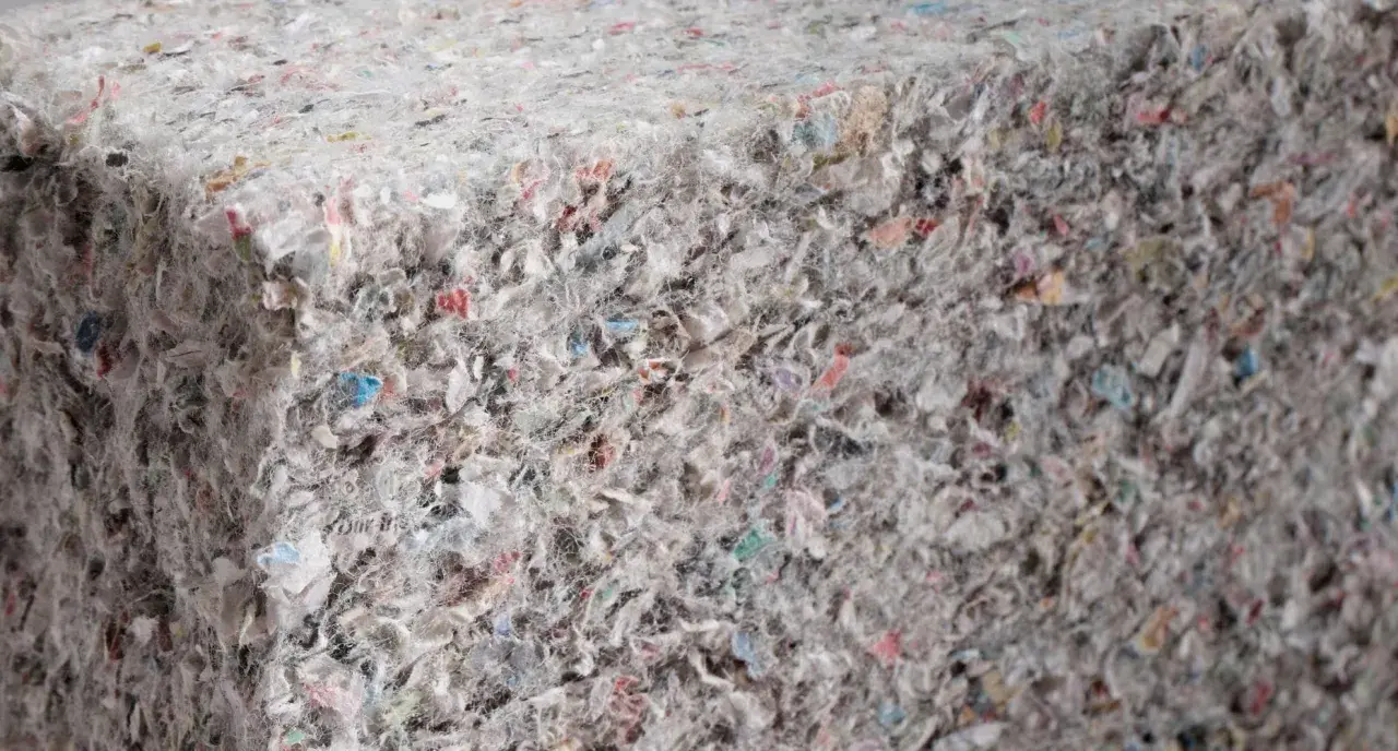 Materiały budowlane: celuloza ocieplenie z recyklingu, tworzące zwartą, włóknistą strukturę z kolorowymi fragmentami.