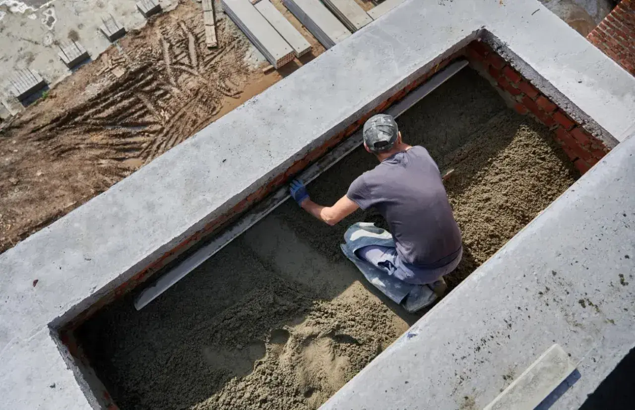 Budowlaniec wyrównuje podsypkę piaskową w wykopie fundamentowym.