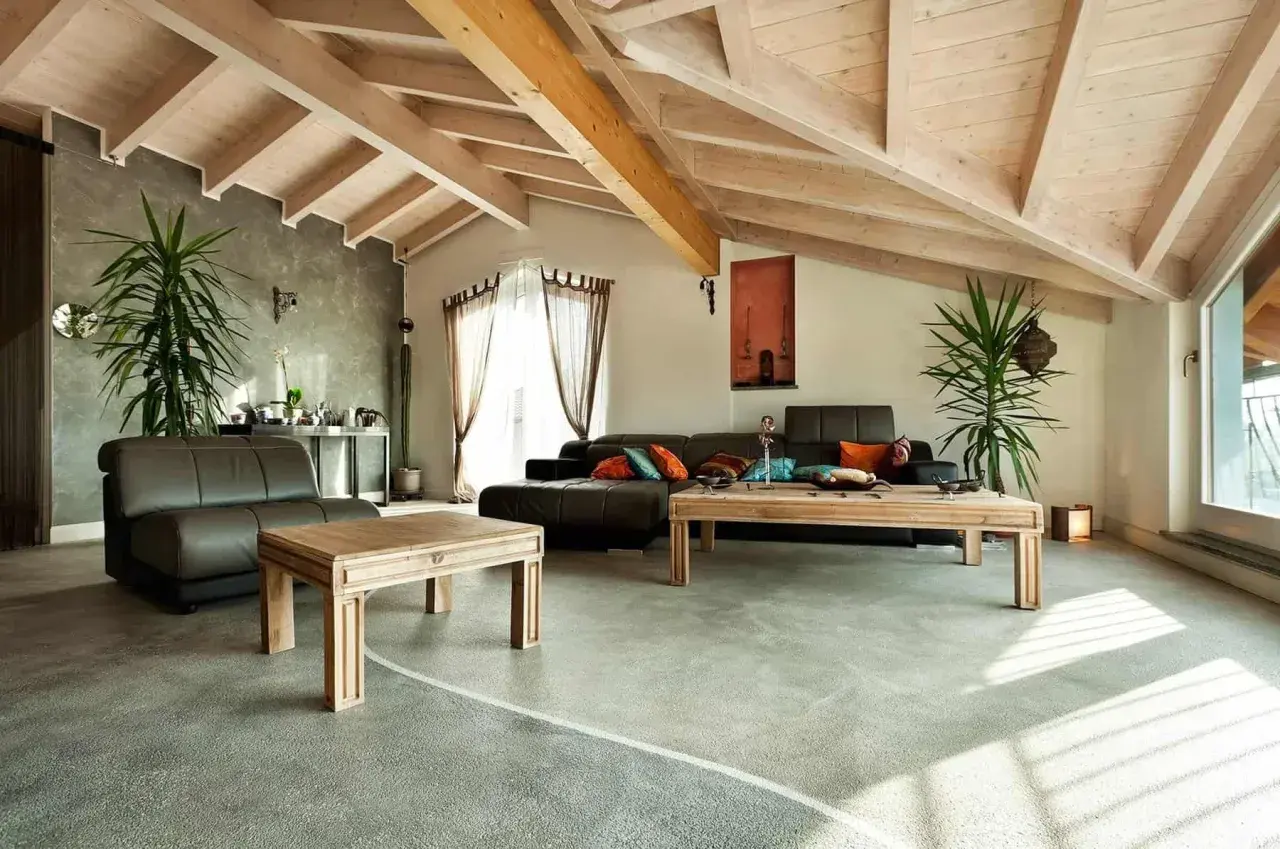 Nowoczesny salon z drewnianym sufitem i posadzką żywiczną w domu. Skórzane kanapy, drewniane stoliki i rośliny tworzą przytulną atmosferę.