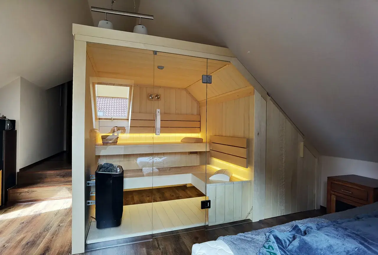 Nowoczesna sauna w domu, wykonana z jasnego drewna, z przeszklonymi drzwiami i nastrojowym oświetleniem. Idealne miejsce na relaks.