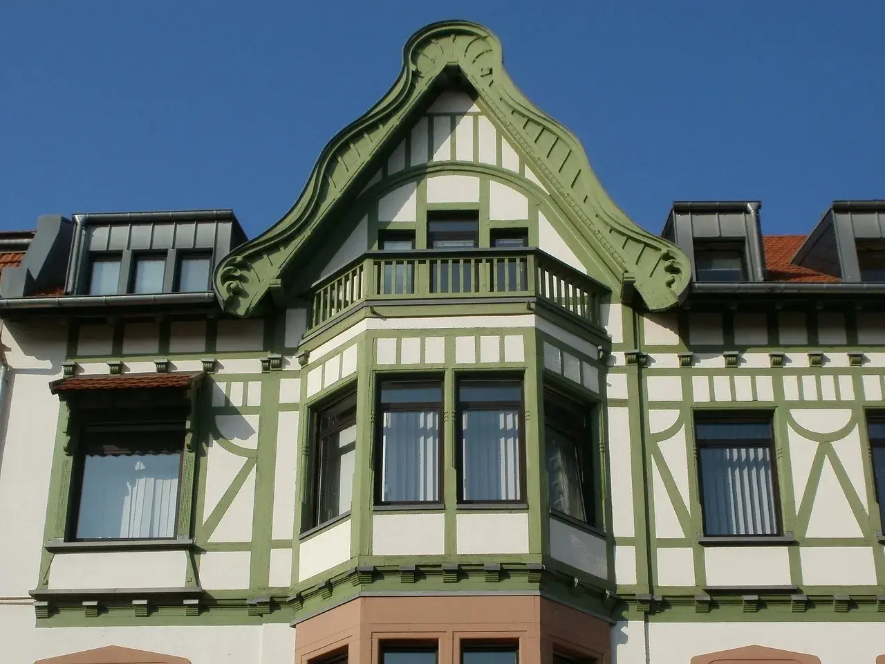 Elegancki ryzalit co to? Wystający fragment fasady budynku, ozdobiony zielonymi elementami i balkonem, z charakterystyczną, falistą formą dachu.