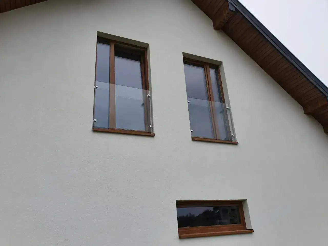 Dwa okna z drewnianymi ramami i szklanymi balustradami na białej ścianie domu.