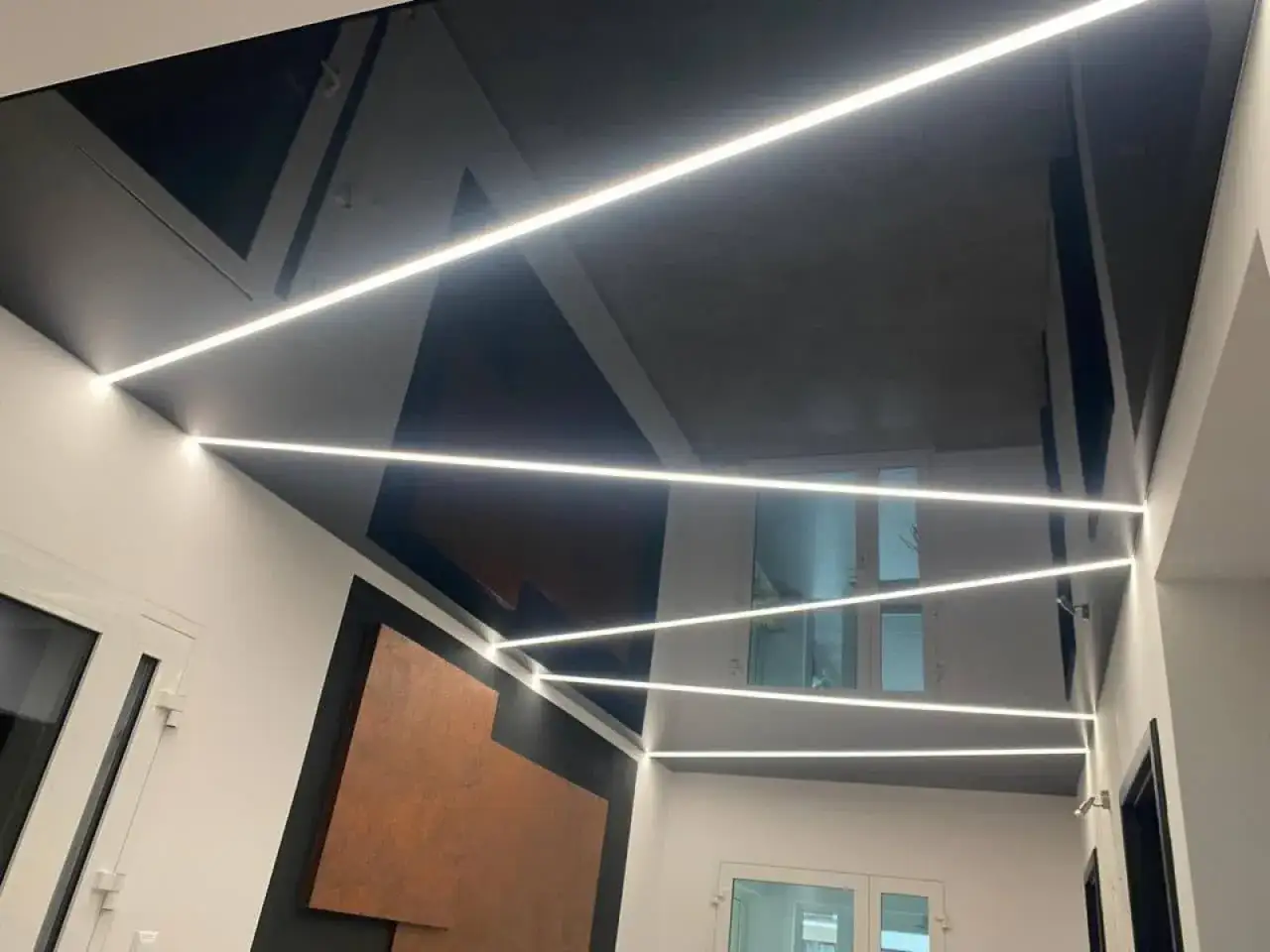 Nowoczesny sufit napinany w kolorze czarnym, z geometrycznymi wstawkami i liniowym oświetleniem LED, tworzącym efektowną grę światła.