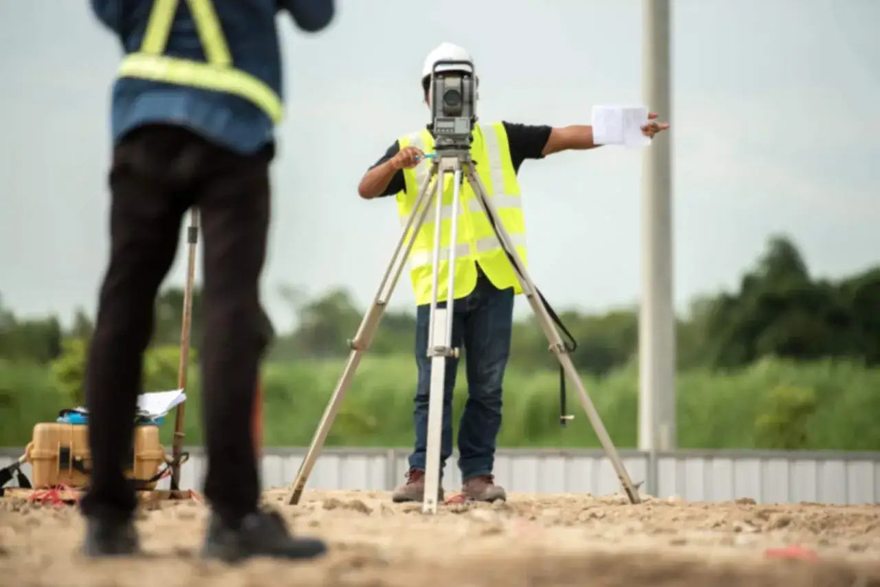 Technik geodeta w kamizelce odblaskowej pracuje z niwelatorem, wyznaczając punkty na budowie.