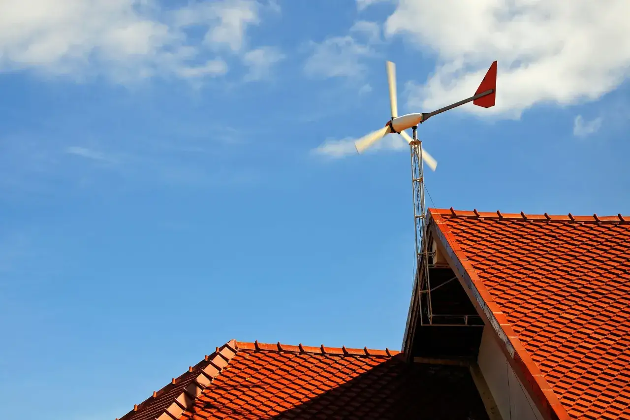 Mały wiatrak na dachu, wykorzystujący energię wiatru, na tle błękitnego nieba z chmurami.