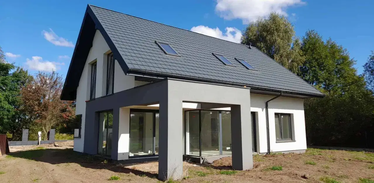 Nowoczesny dom 220m2 w trakcie budowy. Szary dach, białe ściany, duże okna i zadaszenie. Realizacja marzeń o własnym domu.