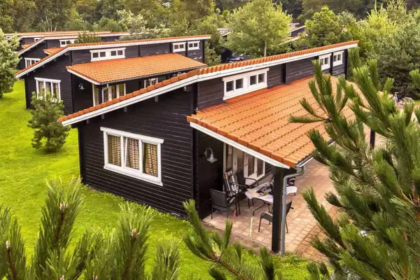 Czarny bungalow z pomarańczowym dachem, otoczony zielenią. Idealne miejsce na wypoczynek, zastanawiasz się bungalow co to?