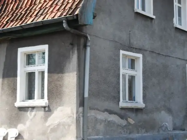 Szare ściany domu z białymi, tradycyjnymi okna skrzynkowe. Dach pokryty czerwona dachówką.