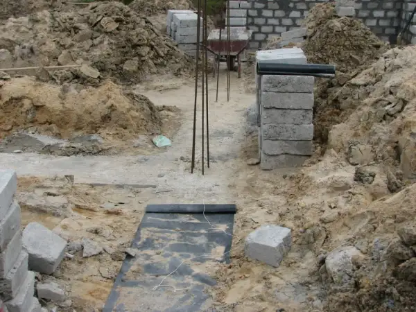 Budowa domu w toku. Widać wykopy, zbrojenie i materiały budowlane. Fundament czeka na zalanie.