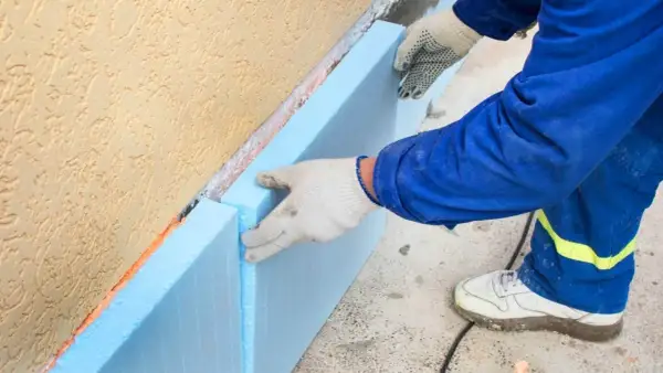 Ręce w rękawiczkach układają niebieski styropian na fundamencie. To kluczowy etap budowy, by wybrać odpowiedni styropian na fundament.