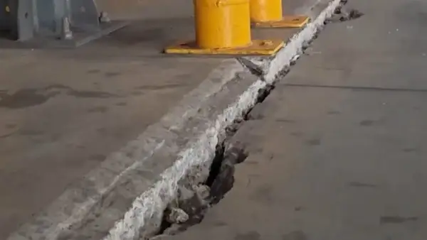 Pęknięcie w betonowej posadzce z widocznymi podporami przemysłowymi w tle.