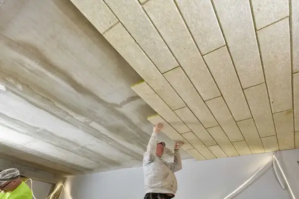 Pracownicy montują płyty izolacyjne, wykonując ocieplenie stropu betonowego.