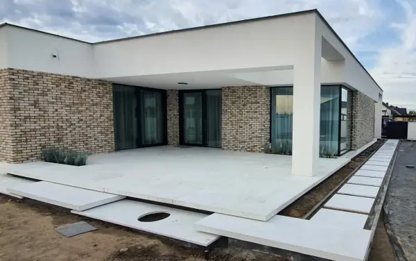 Nowoczesny dom z ceglaną elewacją i tarasem z jasnego, **betonu szczotkowanego**.