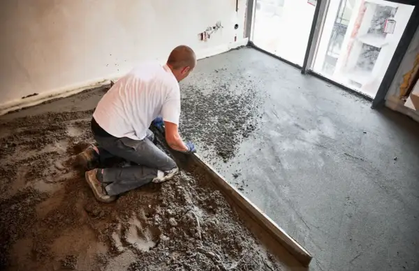 Budowlaniec wyrównuje świeżą wylewkę anhydrytową na podłodze, używając łaty.