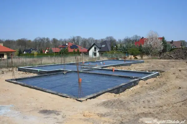 Fundament płyty fundamentowej w budowie, z czarną folią i zbrojeniem.