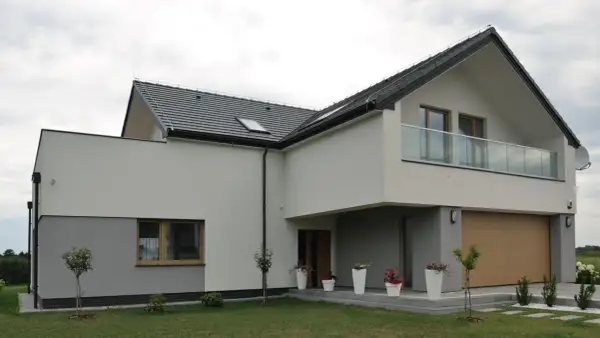 Nowoczesny dom z dwuspadowym dachem i balkonem. Elewacja w odcieniach bieli i szarości, z drewnianą bramą garażową. Świetny pomysł na elewację domu.